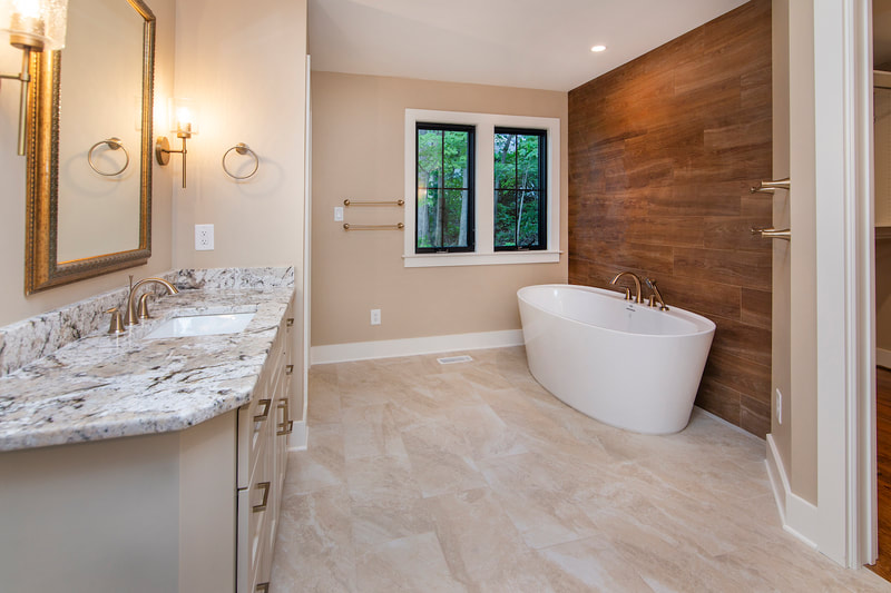 Lake Forest Lodge custom renovation master bathroom with vanity sink and large soaking tub by windows with views of the forest