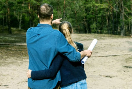Couple looking at undeveloped plot of land with plans to build a custom home