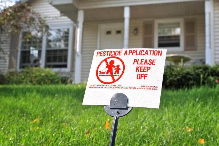 Pesticide application warning sign in green lawn in front of house.