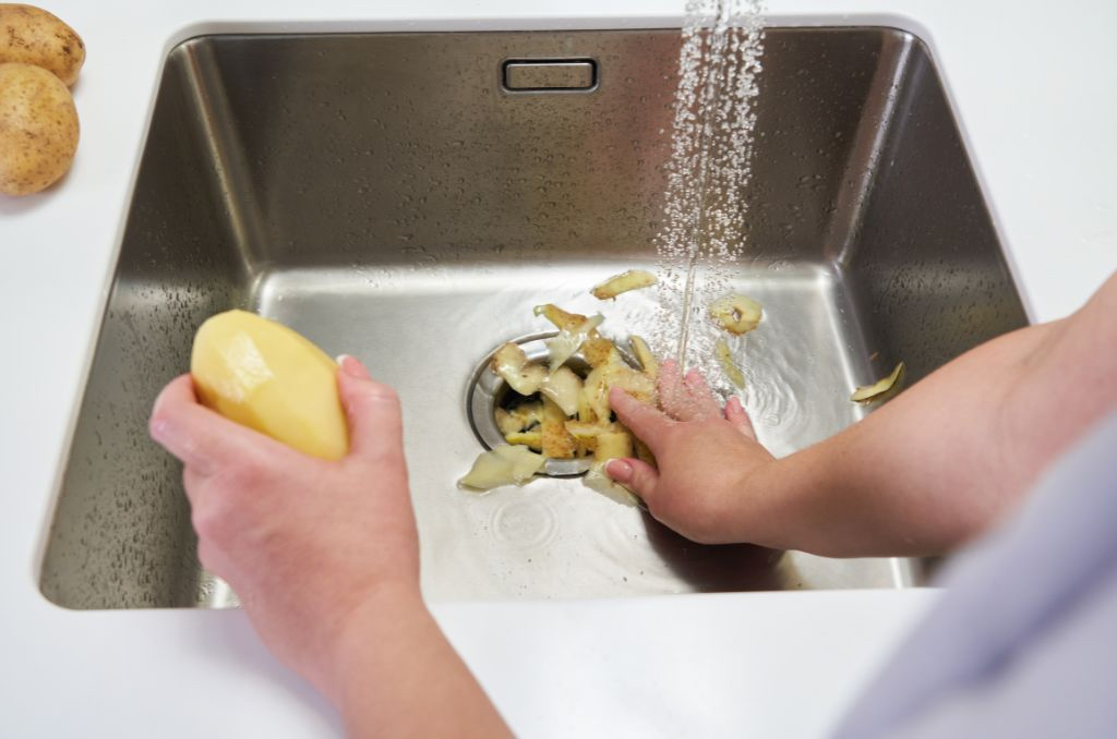 Man putting potato peelings down garbage disposal at sink
